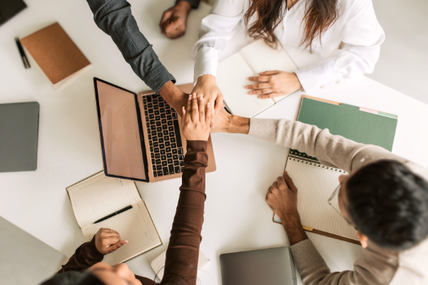 Team legt im Meeting gemeinsam die Hände zusammen als Symbol für Vertrauen, Zusammenhalt und psychologische Sicherheit
