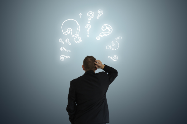 Person in Anzug steht vor Fragezeichen und wirkt unentschlossen.