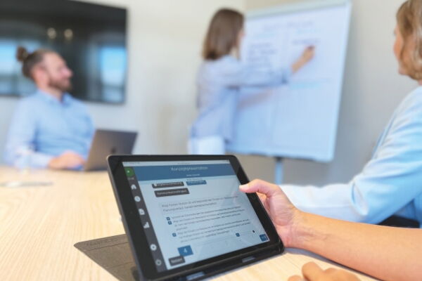 Tablet mit AC-Smart während einer Trainee-Diagnostik, im Meeting werden Ergebnisse am Whiteboard diskutiert